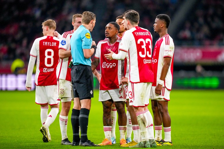 Spelers van Ajax staan vol verbazing rondom scheidsrechter Sander van der Eijk, die zojuist rood heeft gegeven aan Steven Bergwijn.
