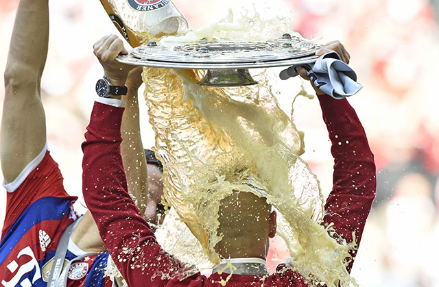 Daniël van Buyten trakteert Pep Guardiola op een bierdouche. Hij probeert zich nog te beschermen met de kampioensschaal, maar dat blijkt zinloos.