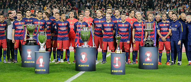 De selectie van Barcelona poseert vóór de wedstrijd tegen Real Betis met de vijf gewonnen prijzen in 2015: de landstitel, de Copa del Rey, de Champions League, de Europese Super Cup en het WK voor clubs