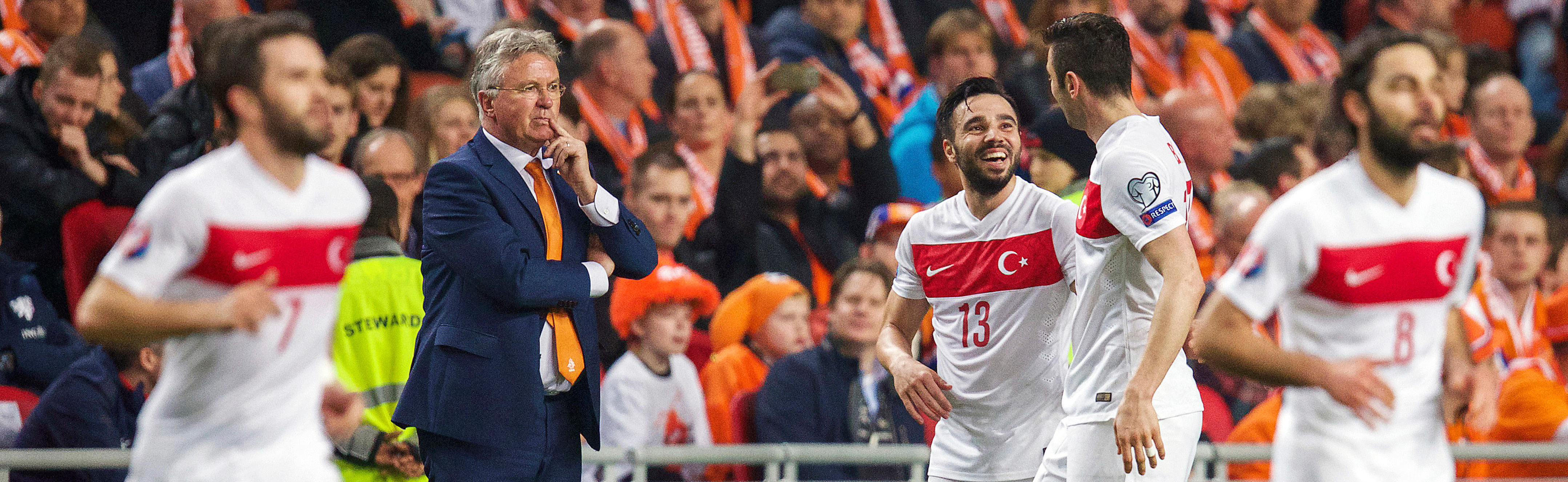 Tussen de feestende Turken kijkt Hiddink bedenkelijk. Hoe krijgt hij Oranje weer aan de praat?